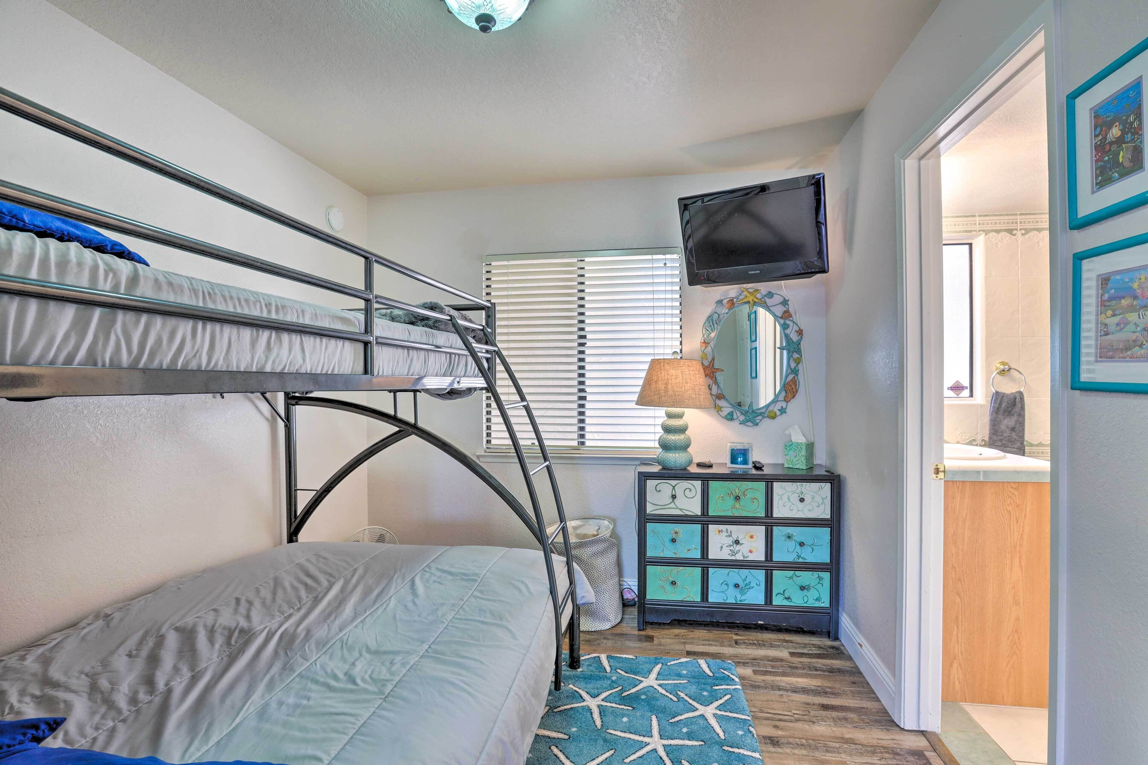 A bedroom with bunk beds, a television, a dresser, and a window with blinds.