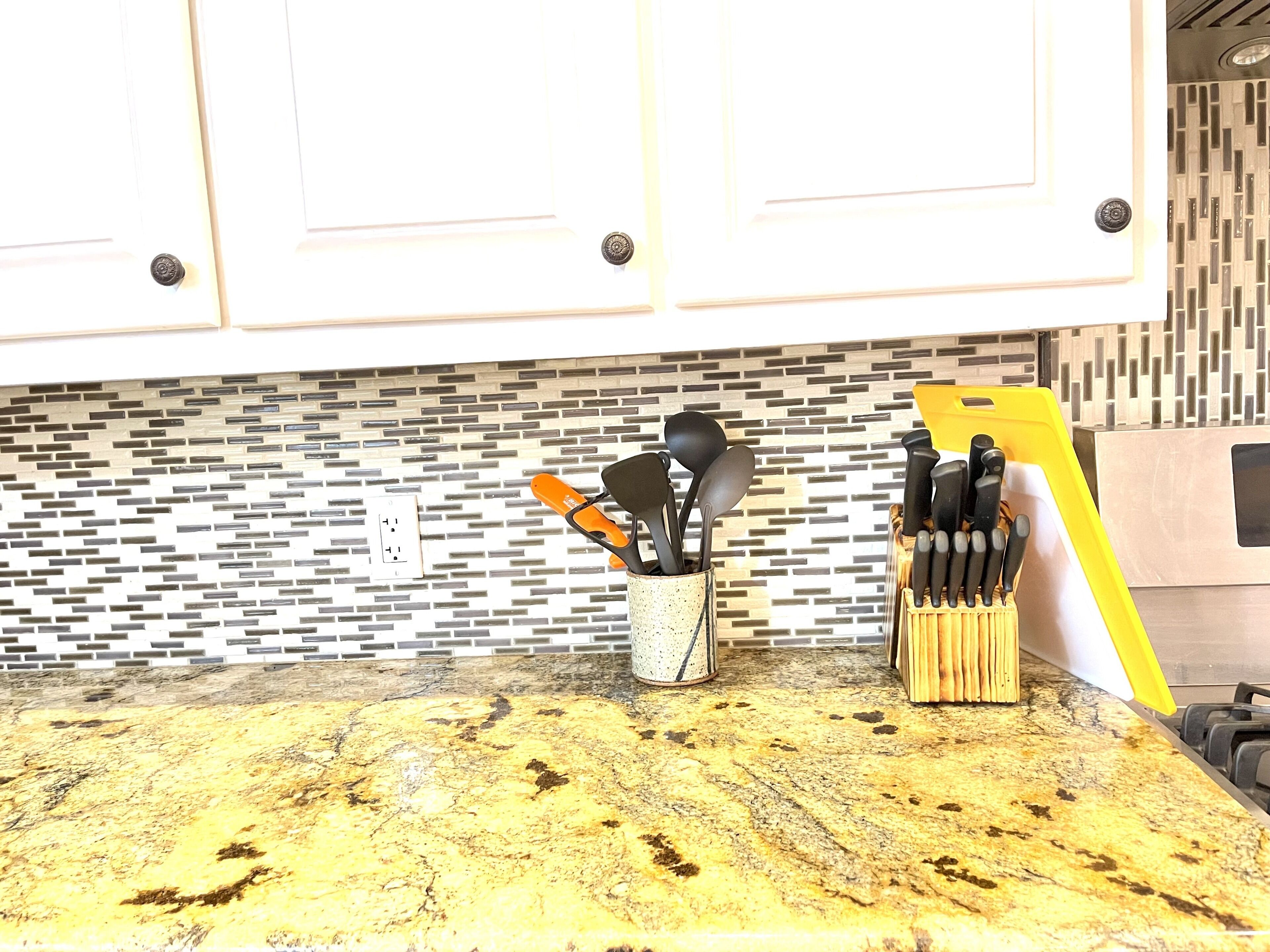 A kitchen counter with a granite top, a knife block, and a utensil holder.