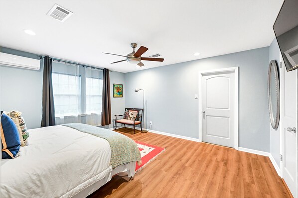 A bedroom with a bed, a chair, a ceiling fan, and a door.