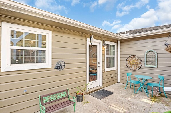 Une maison avec un revêtement extérieur de couleur beige, une porte d’entrée, un banc et un petit espace patio avec une table et des chaises.