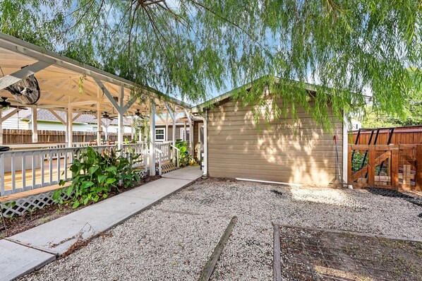A covered patio area with a fan, a wooden fence, and a gravel driveway.