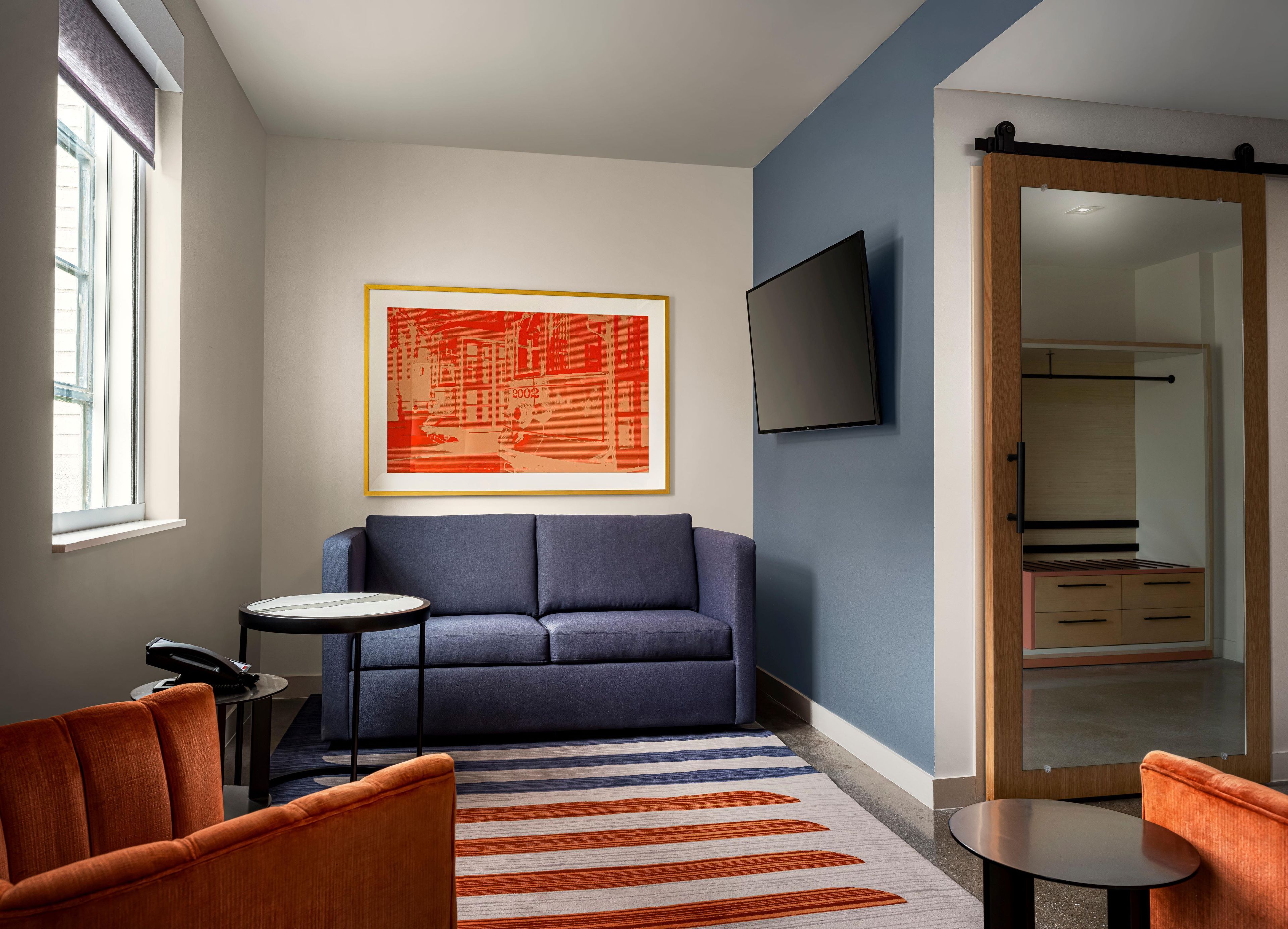 A modern living room with a sofa, a small round table, a striped rug, a framed artwork, and a television mounted on the wall.