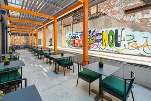 Ein Straßencafé mit Tischen und Stühlen, einer Wandmalerei und Blick auf die Straße.
