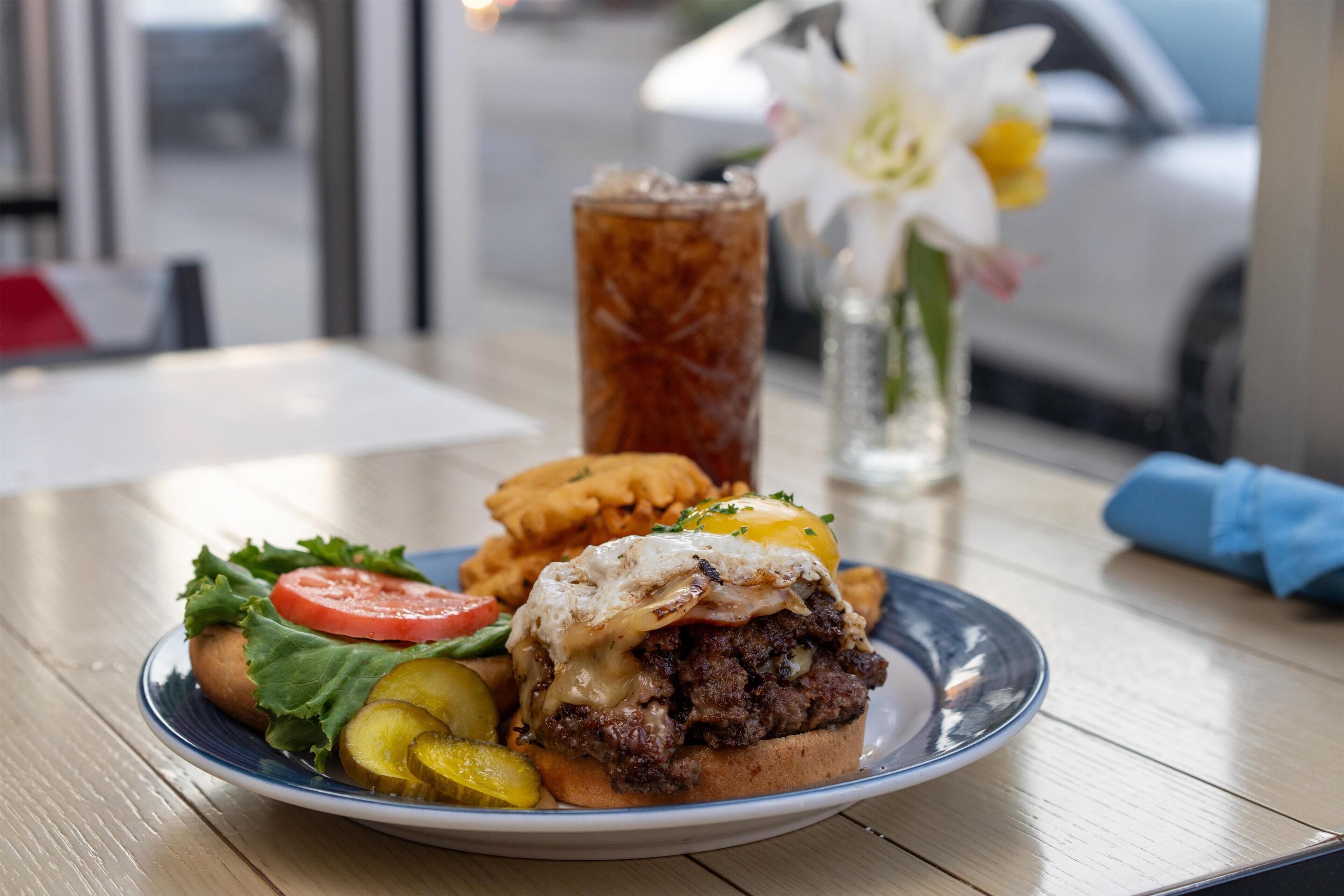 A meal consisting of a burger, fries, and a drink on a table with a window view.