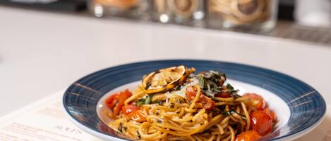 Een bord spaghetti met tomaten en kruiden, geserveerd op een bord met blauwe rand.