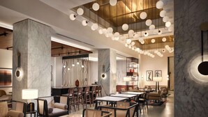 A modern hotel lobby with marble columns, a bar area, and a seating arrangement with tables and chairs. - Canopy by Hilton New Orleans Downtown (New Orleans)