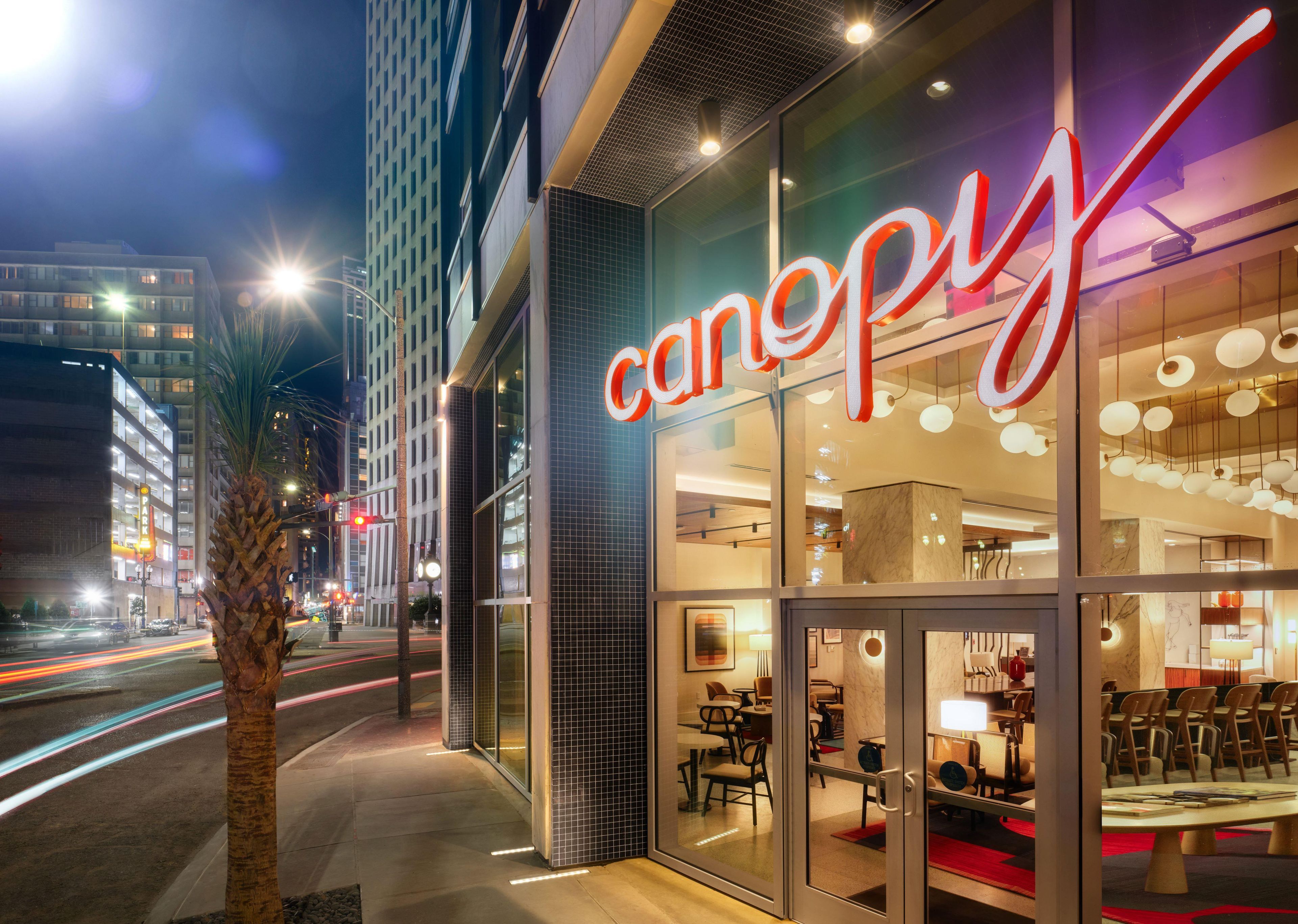 A modern building with a glass facade and a prominent 'canopy' sign. Inside, there are multiple seating areas with tables and chairs.