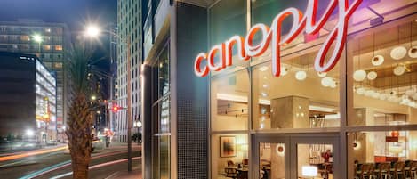 A modern building with a glass facade and a prominent 'canopy' sign. Inside, there are multiple seating areas with tables and chairs.