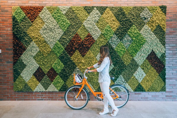 Una persona de pie junto a una bicicleta frente a un muro grande y con diseño.