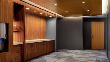 A modern hotel room with wooden cabinetry, a built-in water dispenser, and a patterned carpet.