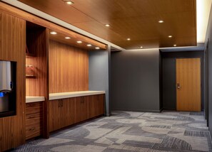 Habitación de hotel moderna con muebles de madera, dispensador de agua integrado y alfombra estampada.