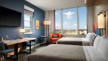 A hotel room with a bed, a desk, a chair, a sofa, a TV, and a large window with a city view.
