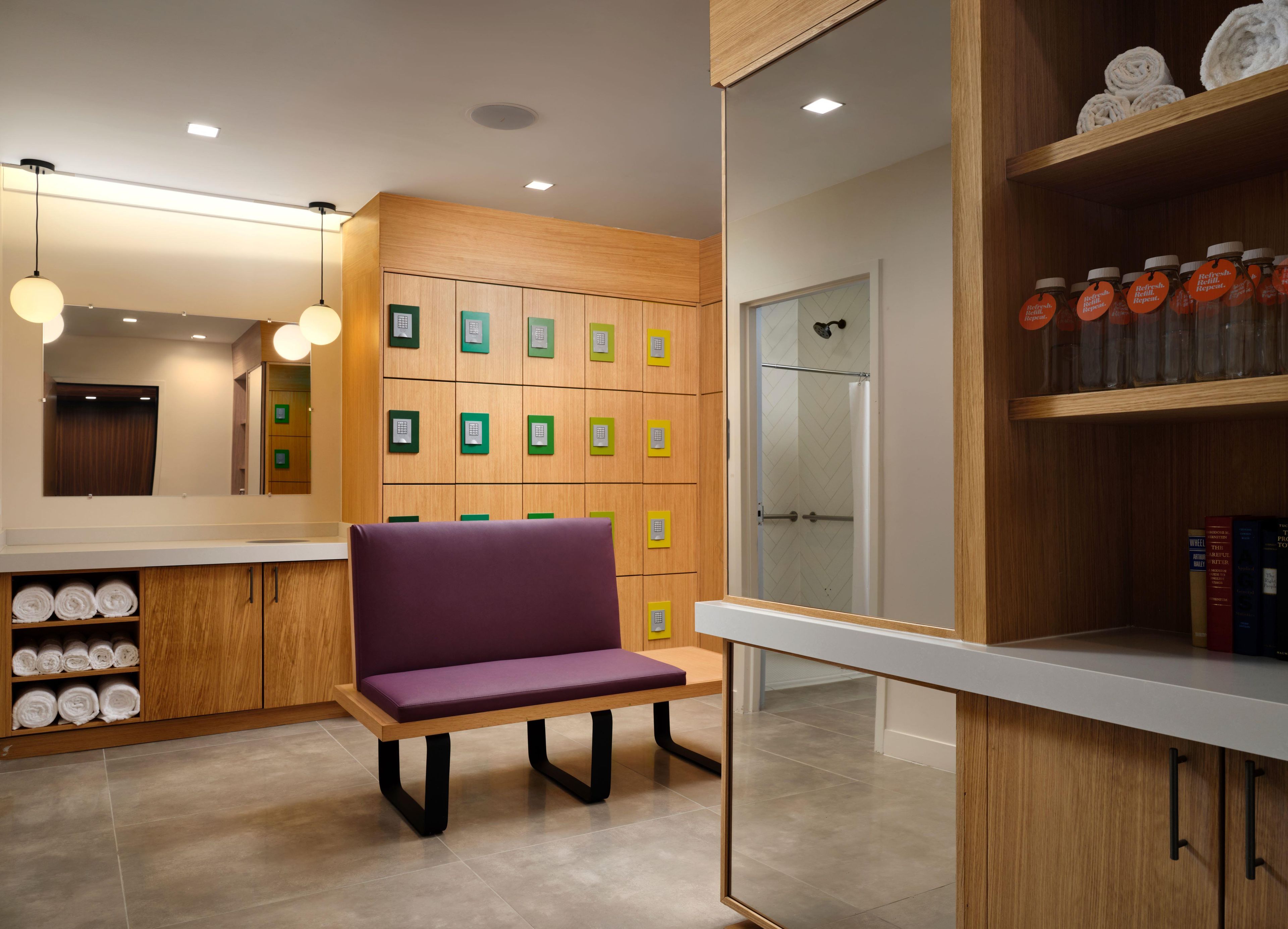 A modern bathroom with wooden cabinets, a purple bench, and a glass shower enclosure.