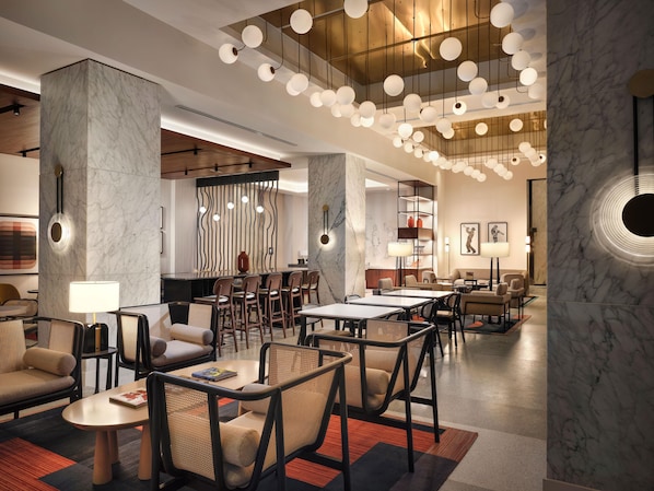 Un moderno vestíbulo de hotel con columnas de mármol, una zona de bar central y un espacio de estar con mesas y sillas.