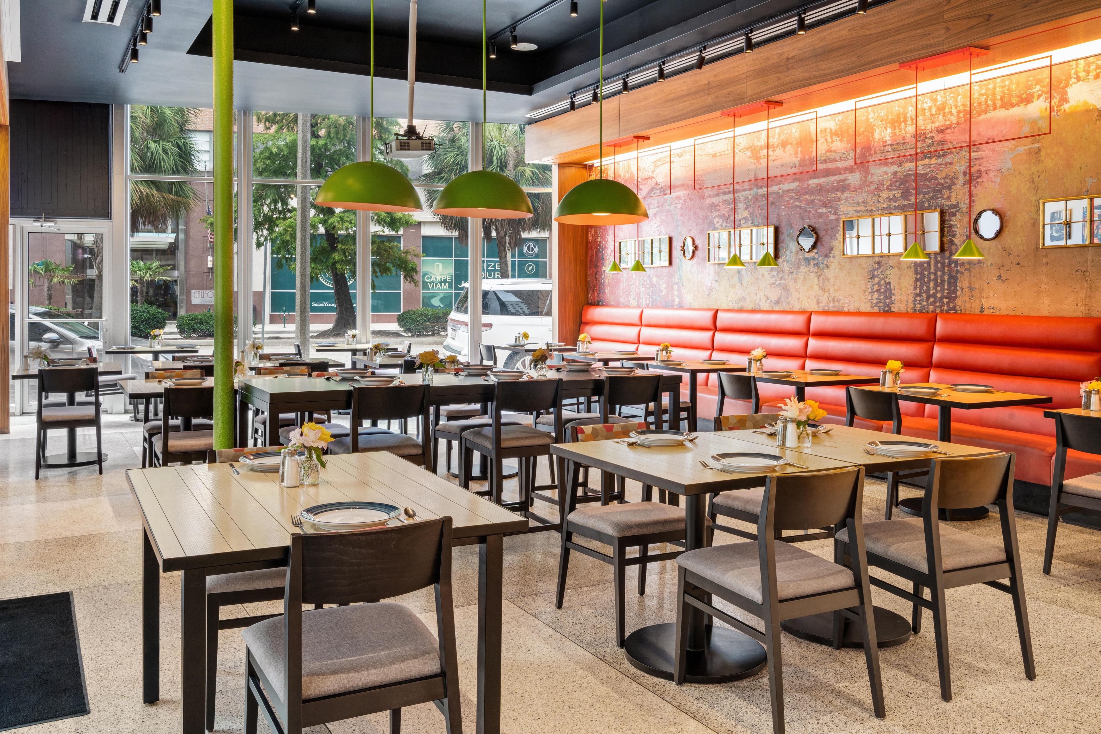A restaurant interior with multiple tables and booths, large windows, and a red accent wall.