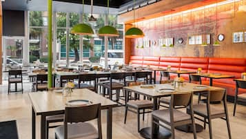A restaurant interior with multiple tables and booths, large windows, and a red accent wall.