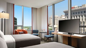 A hotel room with two beds, a desk with a TV, a chair, and large windows offering city views. - Canopy by Hilton New Orleans Downtown (New Orleans)