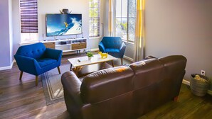 Ein Wohnzimmer mit einem braunen Sofa, zwei blauen Sesseln, einem Couchtisch und einem Fernseher auf einem Schrank.