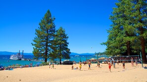 A beach volleyball court with players, a boat docked nearby, and tall pine trees in the background. - Stylish and Bright Home with City, Mountain and Valley Views (Sparks)
