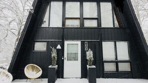 A black double-story house with a white door and windows, surrounded by snow-covered ground and trees. - Vintage Waterfront A Frame- Hideaway On The Bay (Lusby)