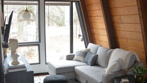 A cozy room with a sloped ceiling, a sofa, ottomans, a small table, and a hanging light fixture. - Vintage Waterfront A Frame- Hideaway On The Bay (Lusby)