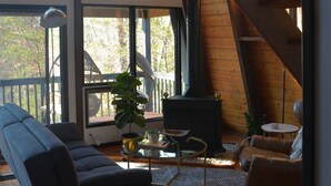 A spacious living area with a large window, a fireplace, a sofa, and a coffee table. - Vintage Waterfront A Frame- Hideaway On The Bay (Lusby)