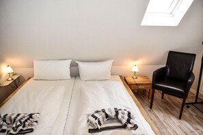 Hotellihuone, jossa on parivuode, kaksi yöpöytää valaisimineen, musta nahkainen nojatuoli ja kattoikkuna vuoteen yläpuolella.