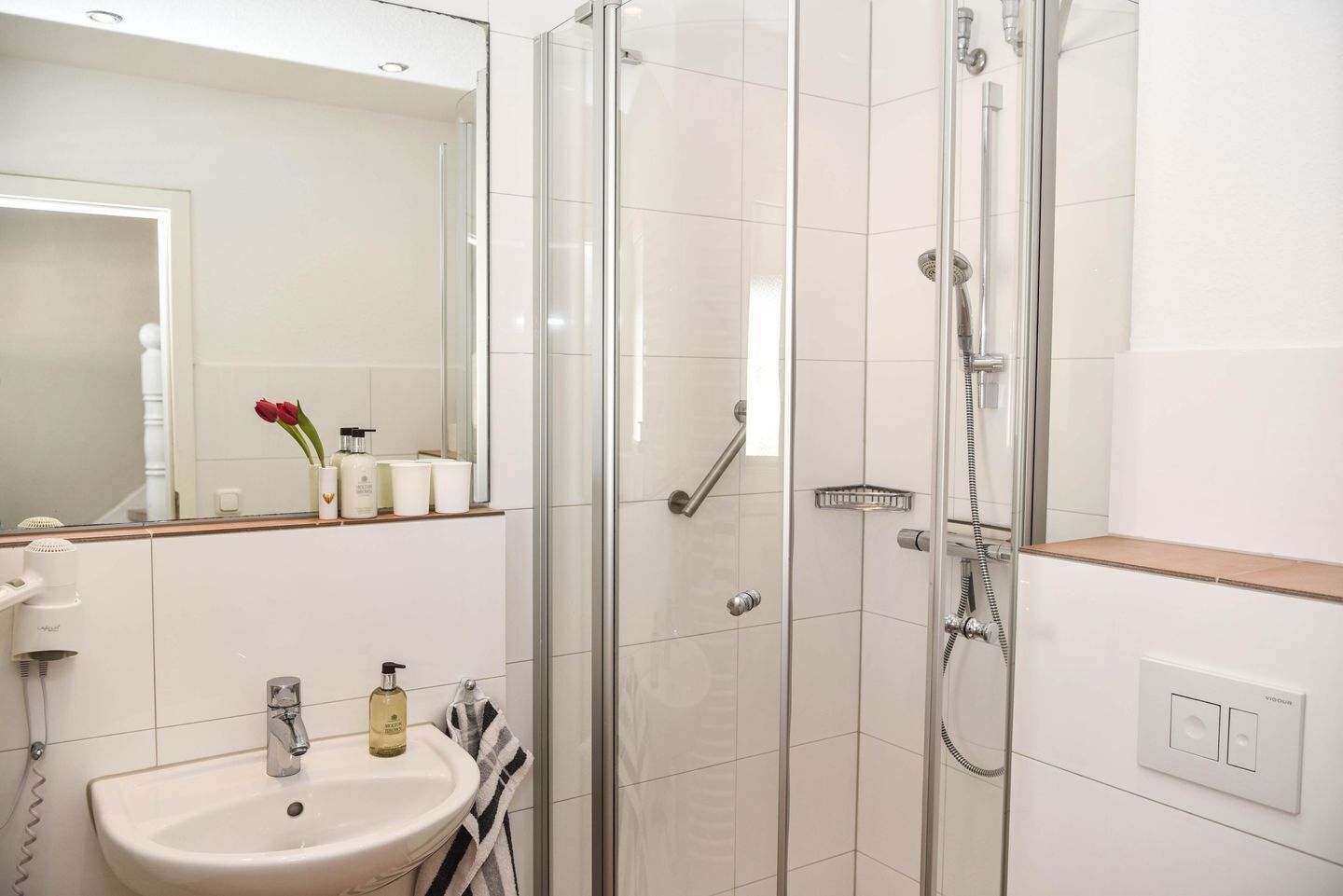 Ein modernes Badezimmer mit einer Glaskabine zur Dusche, einem weißen Waschbecken und einem Spiegel darüber.