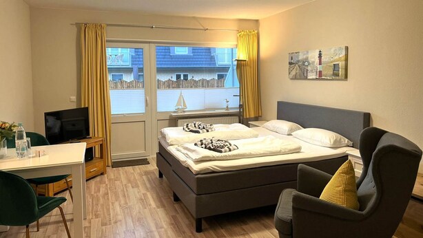 A hotel room with a bed, a desk, a chair, a TV, and a window with curtains.