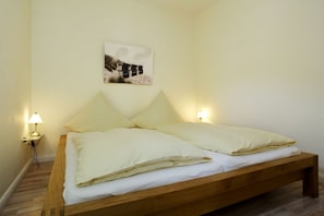 Un lit simple avec un cadre en bois et une literie blanche, deux lampes de chevet et un tableau accroché au mur.
