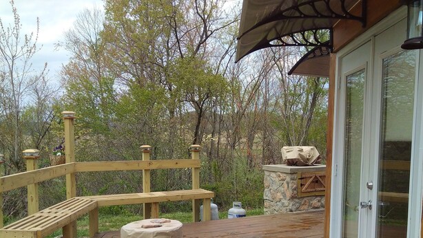 Una terraza de madera con un banco de piedra, un área de estar cubierta y un muro de piedra.