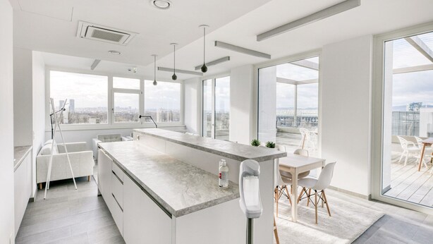 Een moderne keuken met een groot eiland, een eethoek met uitzicht, en een stadsgezicht te zien door grote ramen.
