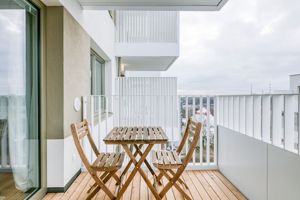 A balcony with a wooden table and chairs, a glass door, and a white railing.