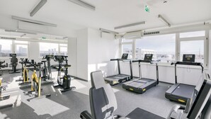Une salle de sport moderne équipée de divers appareils d’exercice, dotée de grandes fenêtres et offrant une vue sur la ville.