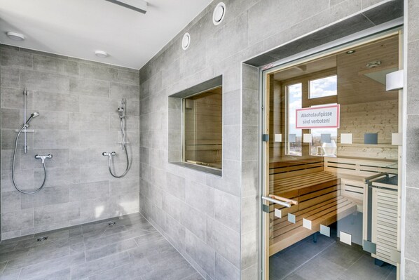 A modern bathroom with grey tiles, a shower area, and a wooden bench with a glass door.