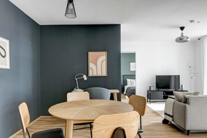 Una sala de estar moderna con una mesa redonda de madera, sofás grises, un televisor de pantalla plana y una pared de acento oscura.