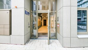 Ein Gebäudeeingang mit Glastür, einem Schild mit der Zimmernummer 330 und einem Feuerschutzschrank links.