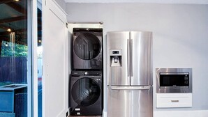 Une cuisine compacte équipée d’un réfrigérateur en acier inoxydable, d’un four à micro-ondes encastré et d’un appareil combinant lave-linge et sèche-linge.