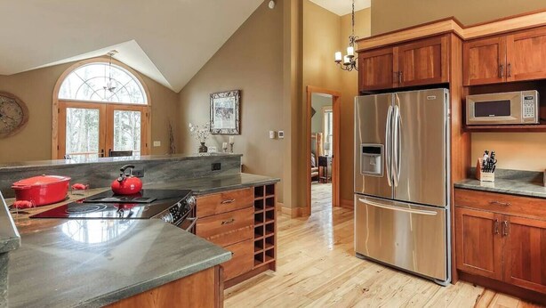 A spacious kitchen with a large island, wooden cabinets, and a stainless steel refrigerator. - Riverbend Retreat with Hot Tub (Traverse City)