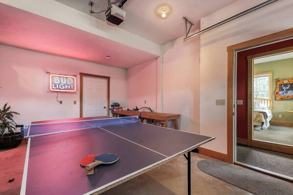 Une pièce avec une table de ping-pong, un néon, une porte et une fenêtre donnant sur un beau paysage.