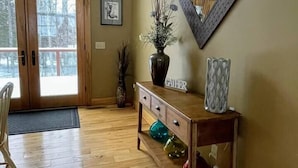 A wooden-floored entryway with a bench, a vase with branches, and a framed mirror on the wall. - Riverbend Retreat with Hot Tub (Traverse City)