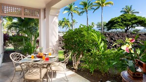 Une terrasse couverte avec une table dressée pour deux personnes, entourée de plantes tropicales et de palmiers.
