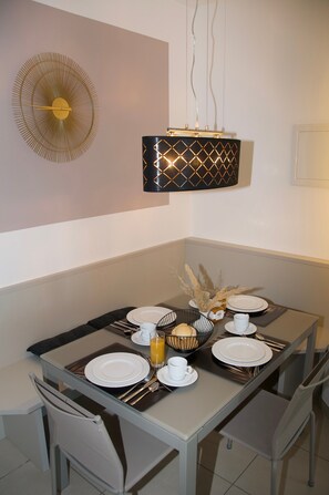 Un comedor con una mesa dispuesta para cuatro, con platos, cubiertos y un vaso de jugo de naranja.