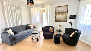 Una sala de estar moderna con un sofá gris, dos sillones, una mesita redonda y una lámpara de pie.