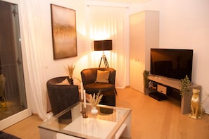 Un salon moderne avec une table basse en verre, un canapé en cuir foncé, un lampadaire noir, un téléviseur à écran plat et une petite statue de chien décorative.