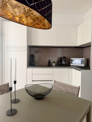 Une cuisine moderne avec des meubles blancs, un four à micro-ondes, une machine à café et un bol posé sur la table.