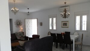 A living room with a sofa, a dining table with chairs, a chandelier, and a door.
