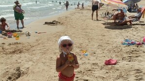 A sandy beach with people, umbrellas, and beach toys.