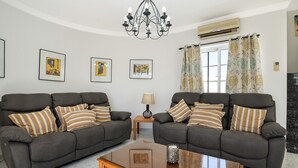 A living room with two sofas, a coffee table, a chandelier, framed artwork on the wall, and a window with curtains. - Villa Sheila – Family Villa with Heated Pool in Puerto del Carmen (Puerto del Carmen)