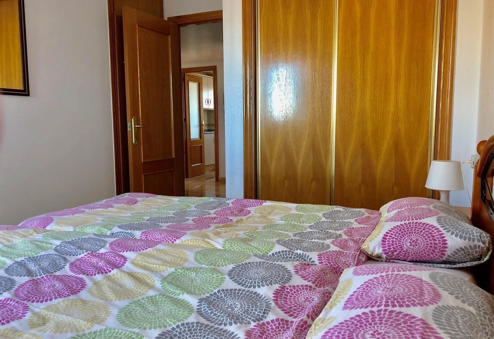 Una habitación con una cama, un armario de madera y una puerta que da a otra estancia.